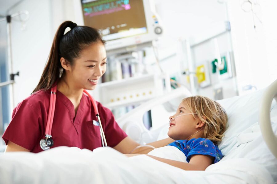 Smiling nurse providing care to a young patient in a hospital bed.