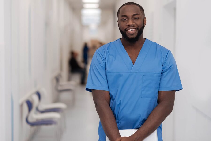 Confident male nurse smiling in a hospital corridor, representing professional healthcare staffing solutions.